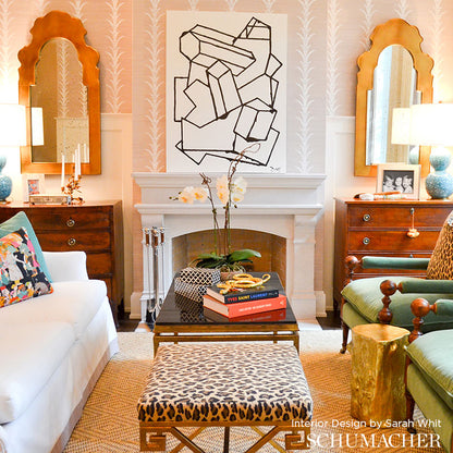 Eclectic living room with leopard-print bench, glass coffee table, pink wallpaper, white fireplace, gold-framed mirrors.