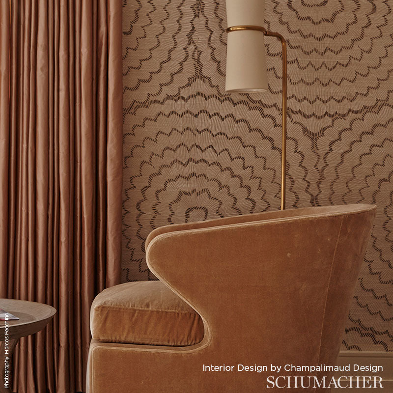 Caramel velvet curved armchair with rounded arms, brass floor lamp, warm patterned wallpaper and rust drapes.