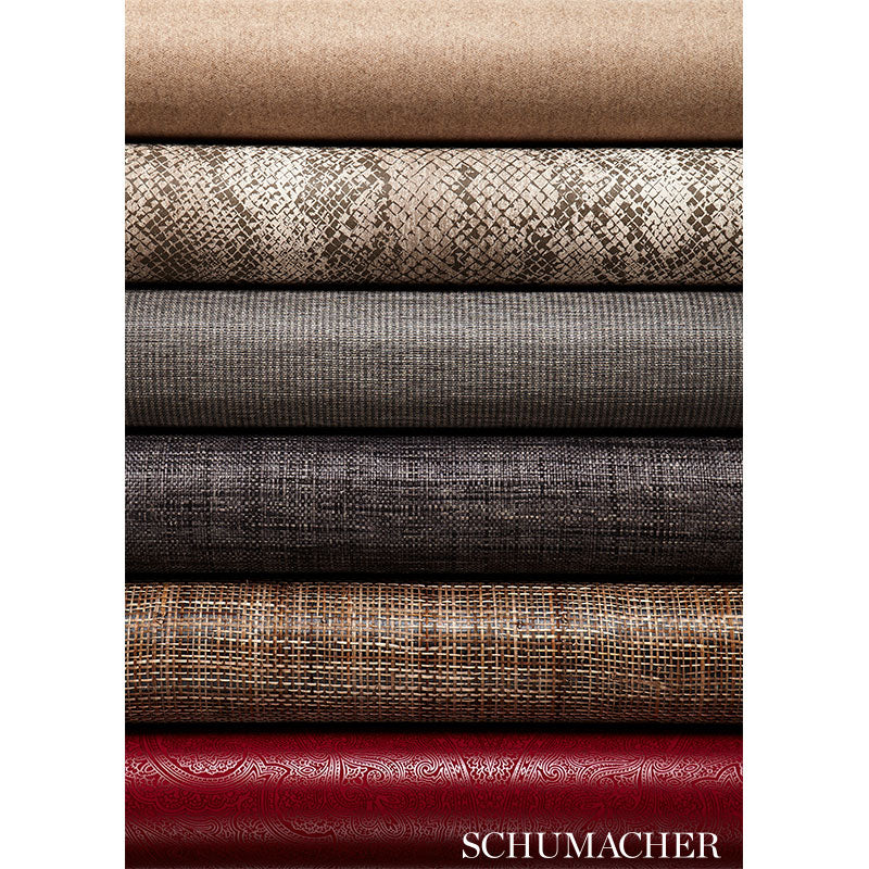Stacked fabric bolts in tan, snakeskin, gray, charcoal, brown weave, and red paisley; Schumacher.