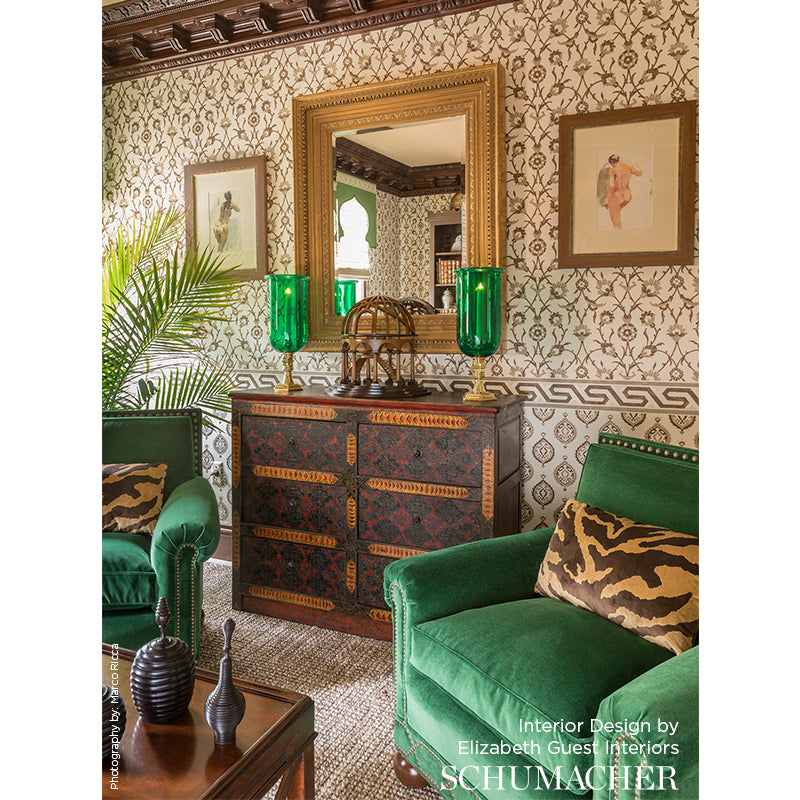 Opulent vintage living room with emerald velvet chairs, tiger-print cushions, ornate dark wood dresser, gold-framed mirror, and green glass lamps.