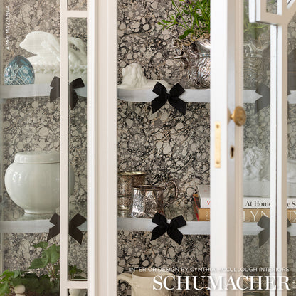 White glass-front cabinet with marble-pattern backdrop, black ribbon bows on shelves, ceramic vase and glassware display.