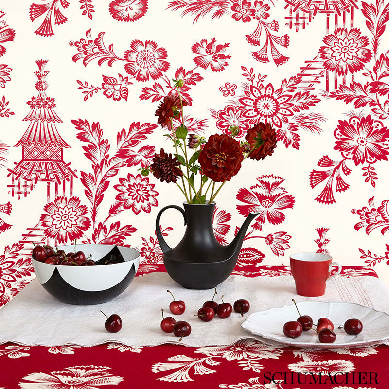 Black porcelain teapot with red carnations, black-and-white bowl, red mug, cherries on a white tablecloth and red wallpaper.