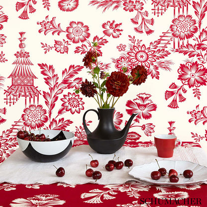 Black porcelain teapot with red carnations, black-and-white bowl, red mug, cherries on a white tablecloth and red wallpaper.