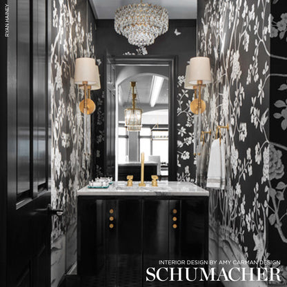 Luxurious black vanity with marble top, gold hardware amid black-and-white floral wallpaper, crystal chandelier and sconces