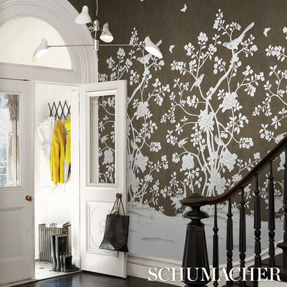Entryway with dark wall and white botanical mural, white doors and arch, wooden staircase banister, black tote bag, coats.