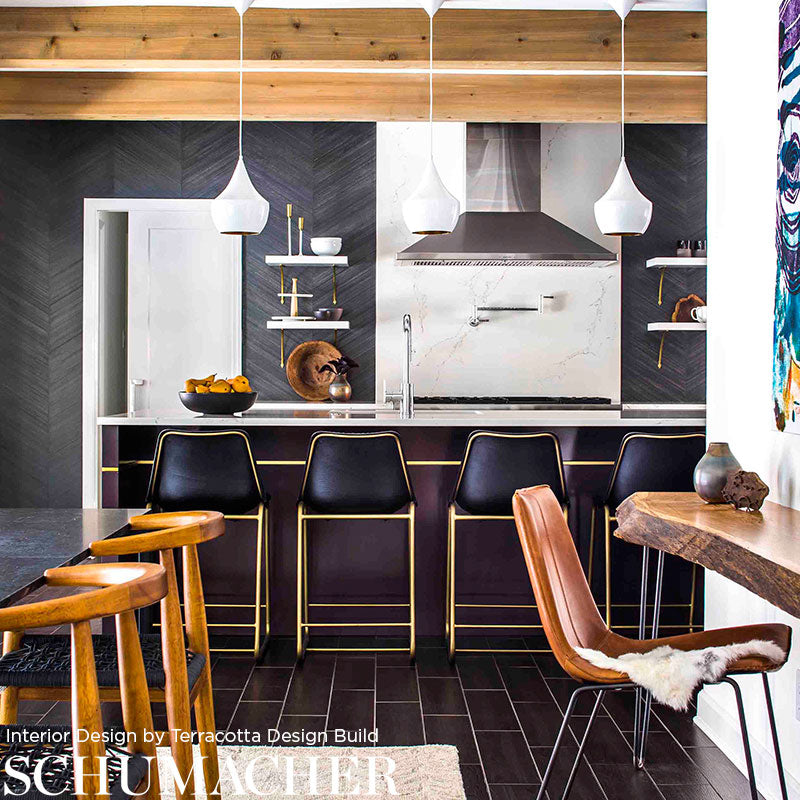 Modern kitchen with dark herringbone cabinets, white countertops, navy stools with gold legs, and faux combed maple chevron flooring.