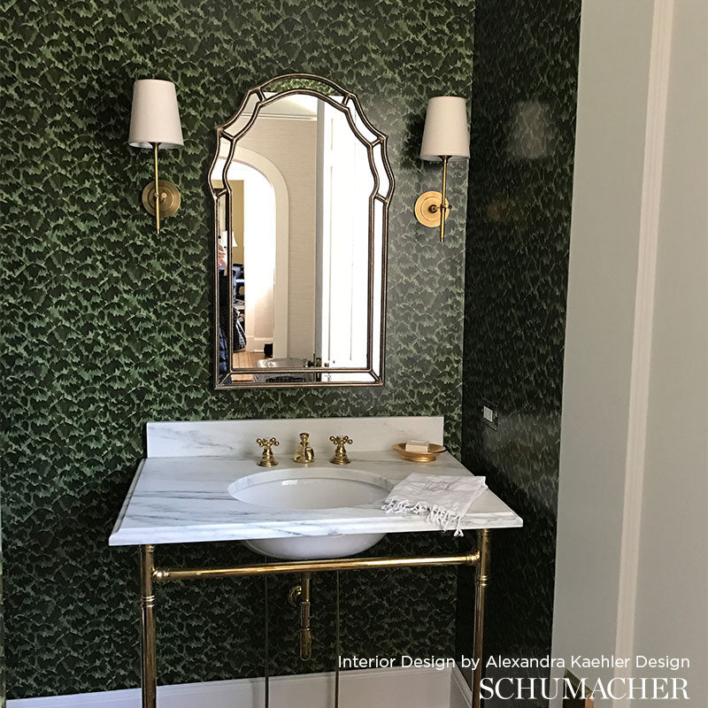 Bathroom vanity with marble countertop, white sink, brass faucet, arched mirror, gold fixtures, green botanical wallpaper.