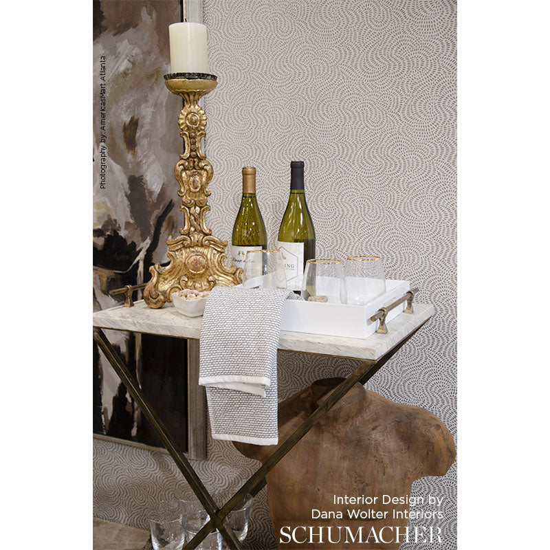 Ornate gold candlestick with white candle, wine bottles and glassware on a white tray with towel atop a decorative bar cart.
