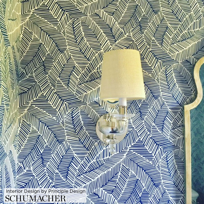 Blue and white palm-leaf patterned wallpaper with a clear glass wall sconce and white fabric shade.