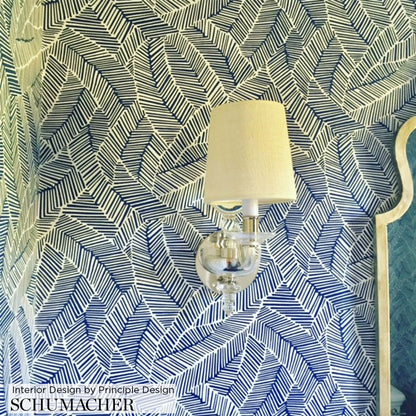 Blue and white palm-leaf patterned wallpaper with a clear glass wall sconce and white fabric shade.