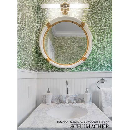 Round gold-framed mirror above a marble bathroom vanity with palm-leaf wallpaper and white wainscoting.