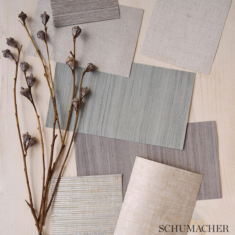Assorted fabric swatches in muted beige, grey, and blue-green tones with dried branches on light wood surface.