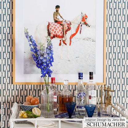 White bar cart with glass liquor bottles, blue stemware, lemons, tall vase of blue delphiniums, framed horse artwork.