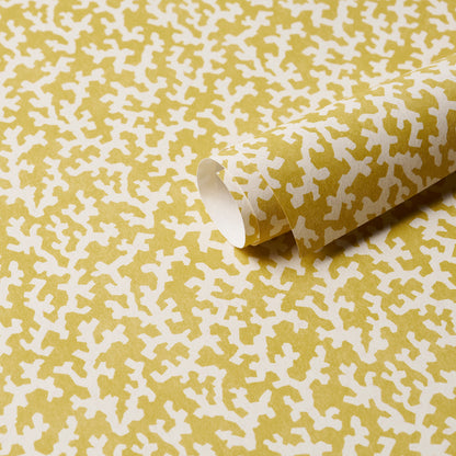 Mustard-yellow wrapping paper with white abstract cross-like pattern; rolled sheet.