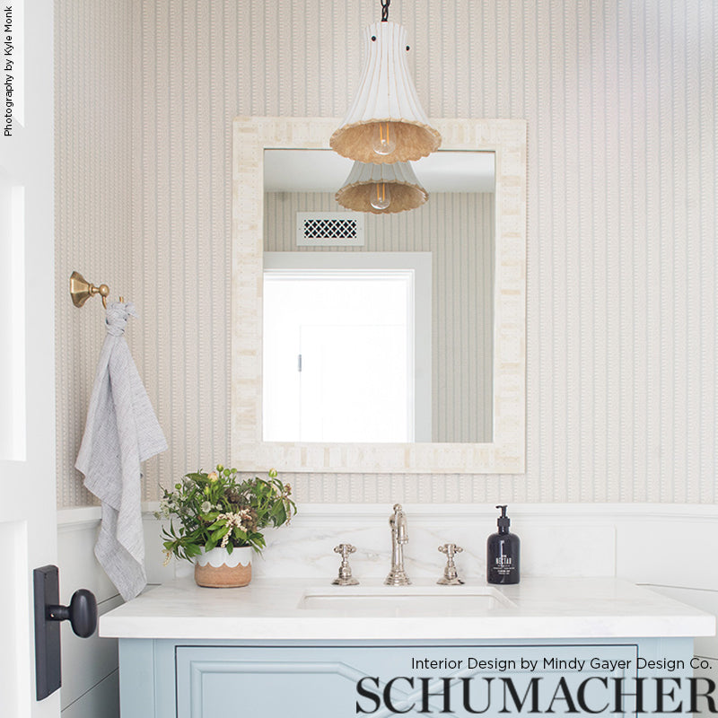 Blue bathroom vanity with white marble top, silver faucet, beige-framed mirror, striped wallpaper, wicker pendant light, plant and towel.