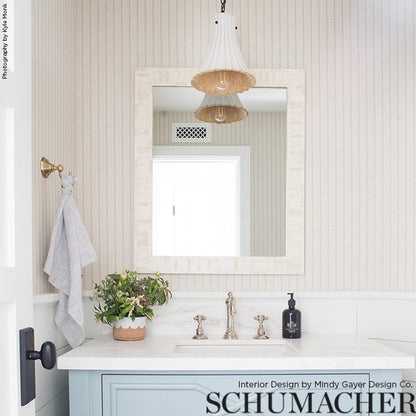 Blue bathroom vanity with white marble top, silver faucet, beige-framed mirror, striped wallpaper, wicker pendant light, plant and towel.
