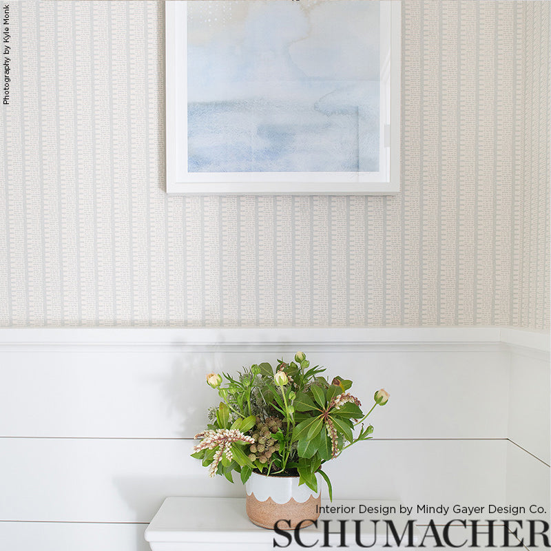 Green bouquet with pink accents in beige ceramic pot on white console beneath patterned wallpaper and framed blue artwork