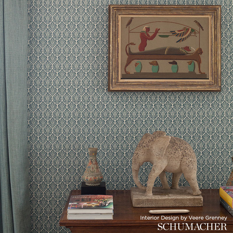 Eclectic interior vignette: framed painting, elephant sculpture, ceramic vase, books on a dark wood table, teal wallpaper.