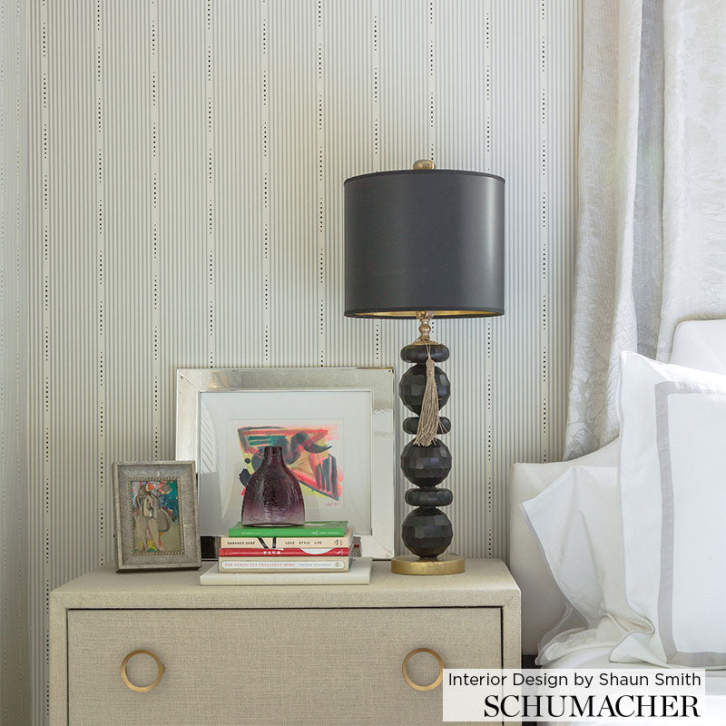 Beige textured bedside table with brass ring pulls, black stacked-ball lamp on a gold base, framed art and books.