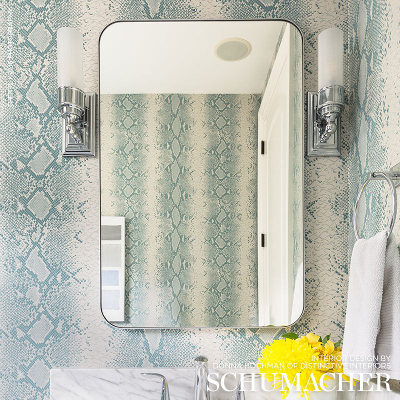 Rounded bathroom mirror with chrome sconces, blue snakeskin wallpaper, marble countertop, white towel ring, modern vanity.