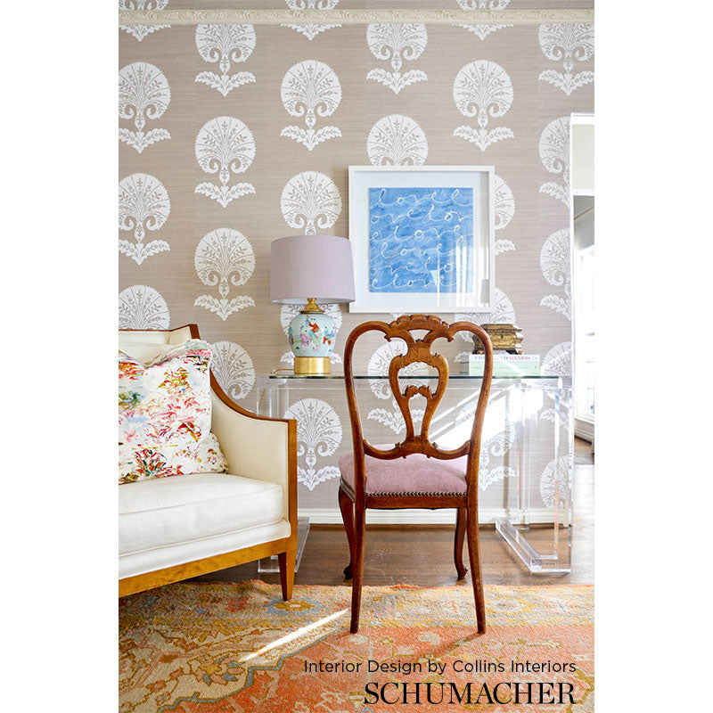 Dark wood carved-back chair with pink upholstered seat beside a glass desk; beige damask wallpaper, floral sofa, blue art.