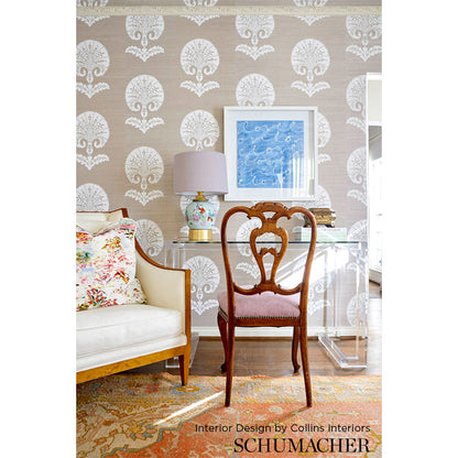Dark wood carved-back chair with pink upholstered seat beside a glass desk; beige damask wallpaper, floral sofa, blue art.