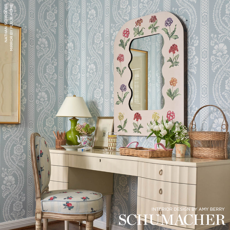 Cream vanity desk with arched floral-bordered mirror, blue damask wallpaper, floral upholstered chair, wicker baskets.
