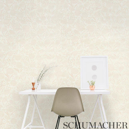 Beige damask wallpaper, white desk with taupe molded chair, framed art, vase of dried grass, and orange-potted plant.