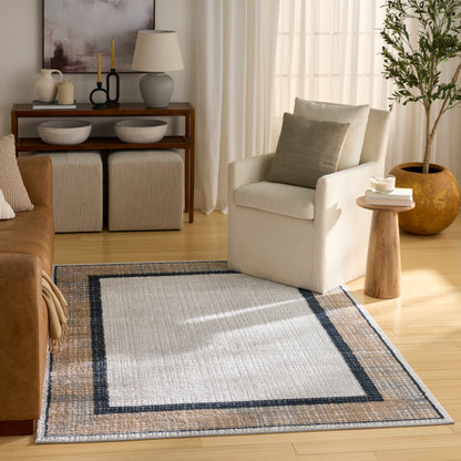 Neutral living room with beige armchair, light wood floor, geometric woven rug with navy border, potted tree, and console.