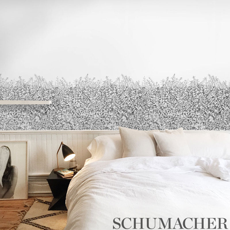Cozy bedroom with white duvet, cream pillows, black bedside lamp, leaning art, and monochrome floral wallpaper.