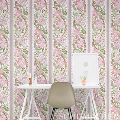 Beige molded chair at white desk set against pink floral striped wallpaper; leaning frame, small plant and vase on desk.