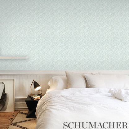 White bed with crisp linens and plush pillows against pale blue patterned wallpaper, black bedside lamp, leaning frame art.
