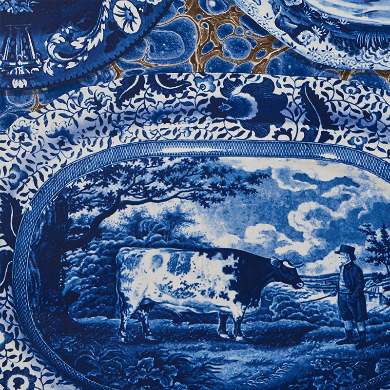 Blue-and-white transferware porcelain plates & platters with a pastoral cow & farmer scene & floral borders.