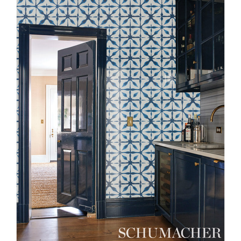 Dark navy kitchen with blue geometric tiled wall, wood floor, wine fridge, gold hardware, open doorway to living area