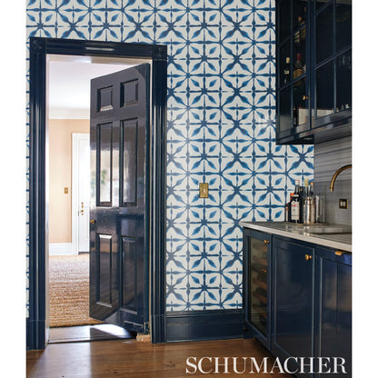 Dark navy kitchen with blue geometric tiled wall, wood floor, wine fridge, gold hardware, open doorway to living area