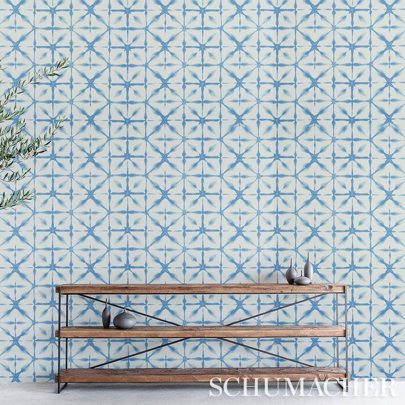 Rustic wood-and-metal console shelves set against blue geometric tile wallpaper, with ceramic decor pieces and a leafy branch on the left.