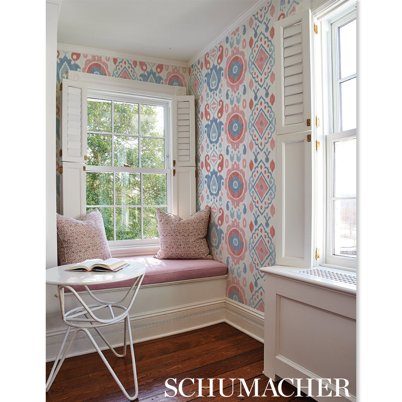 Built-in window seat with pink cushions, white shutters, blue-pink damask wallpaper, and a small white metal table.