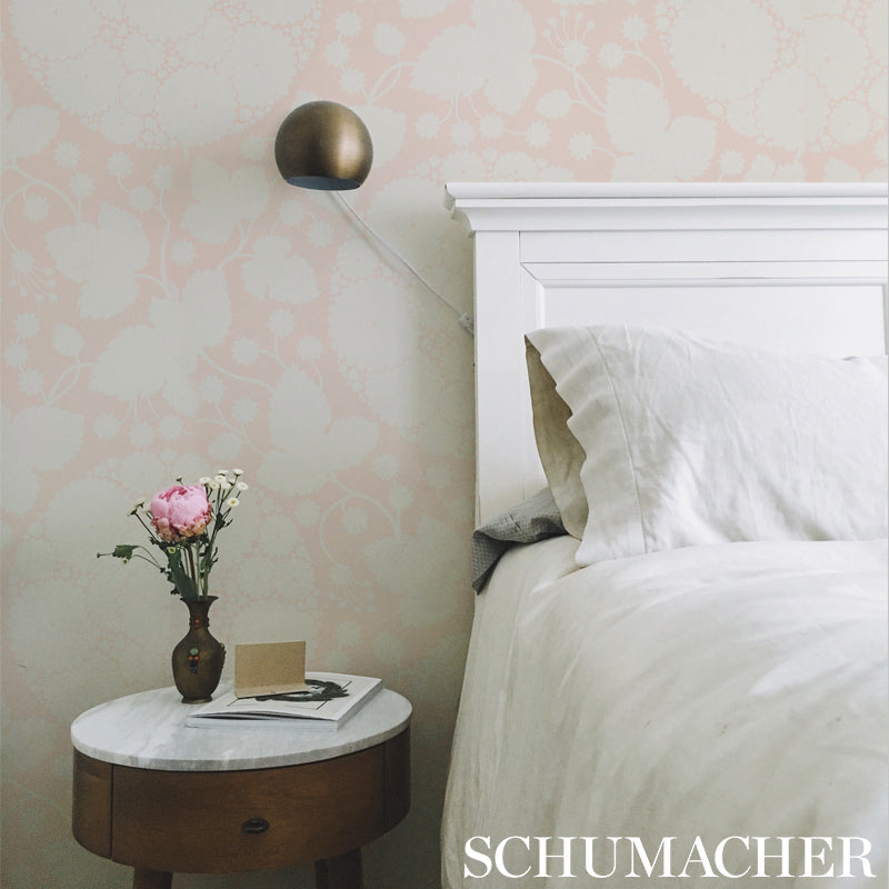 Pastel bedroom scene with white bed, round marble nightstand, pink flowers in vase, brass wall lamp, soft floral wallpaper.