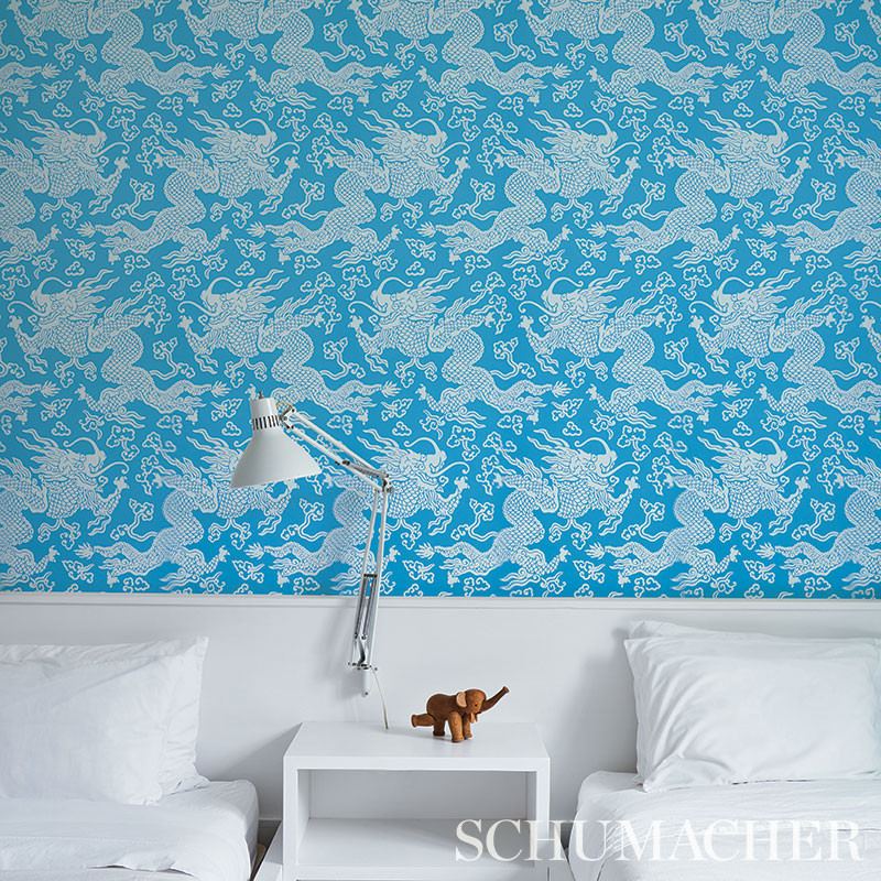 Blue wallpaper with a dragon damask peacock pattern, plus a modern white bedside table, chrome adjustable lamp, and white bed.