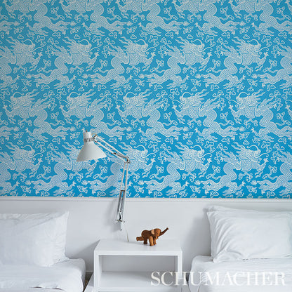 Blue wallpaper with a dragon damask peacock pattern, plus a modern white bedside table, chrome adjustable lamp, and white bed.