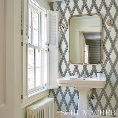 Vintage bathroom with toile-pattern wallpaper; white porcelain pedestal sink and brass-framed rounded mirror.