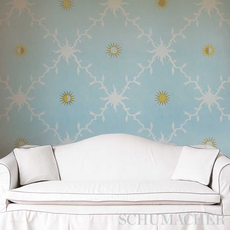 White curved sofa with two matching cushions against pale blue wallpaper with white branch patterns and yellow sun motifs.