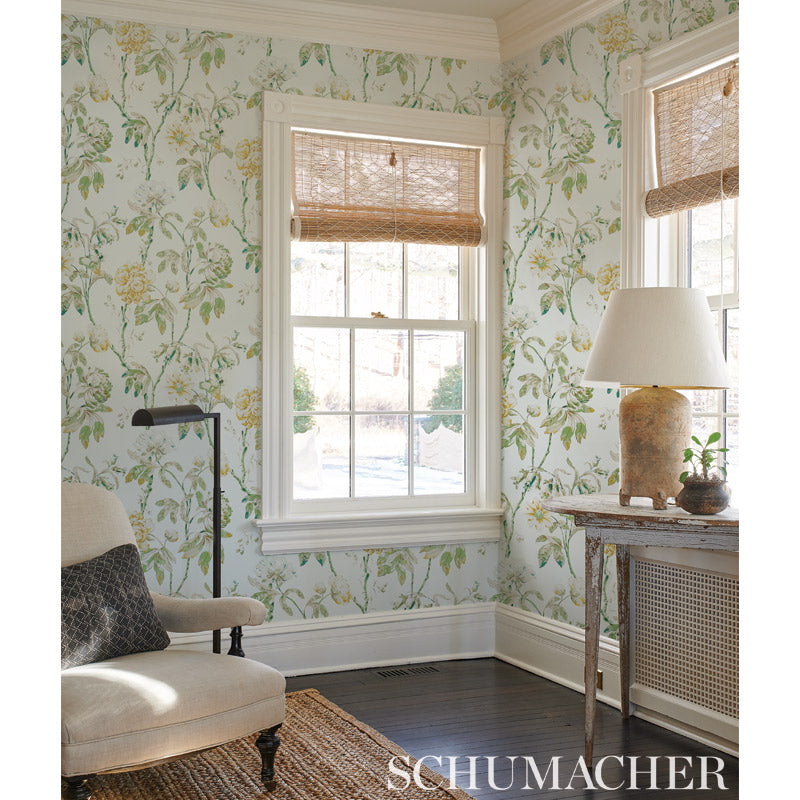 Botanical wallpapered living area with white trim, two windows, woven shades, beige chair, rustic table, lamp and plants.
