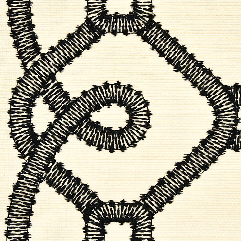 Close-up of thick black braided embroidery forming a geometric diamond pattern on beige fabric.