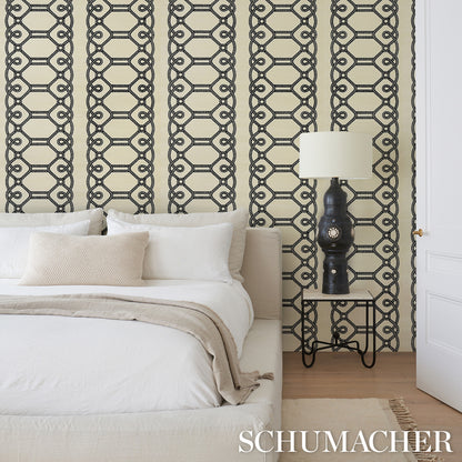 Bedroom with beige geometric chain wallpaper, white bed linens, beige throw, black lamp on metal nightstand, wooden floor.