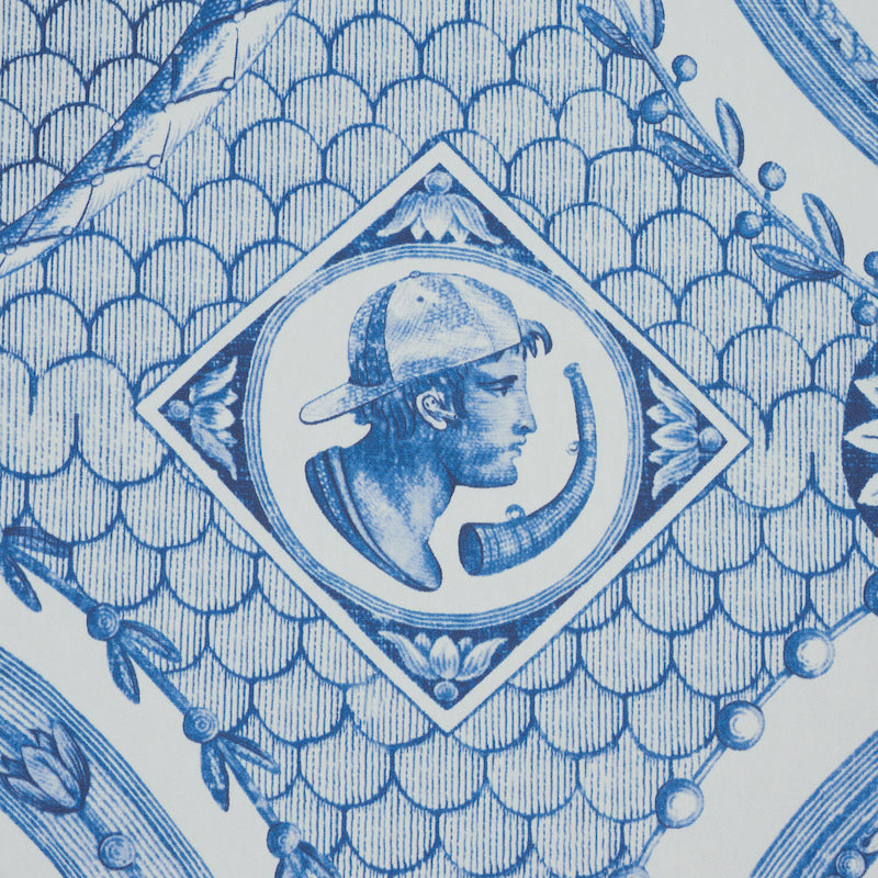 Blue-and-white print with a scalloped scale motif and a diamond medallion featuring a cap-wearing silhouette and a curved object.