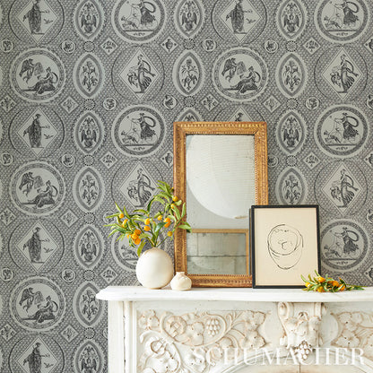Ornate gold-framed mirror on white carved mantel with black-framed sketch and yellow flowers on gray damask wallpaper.