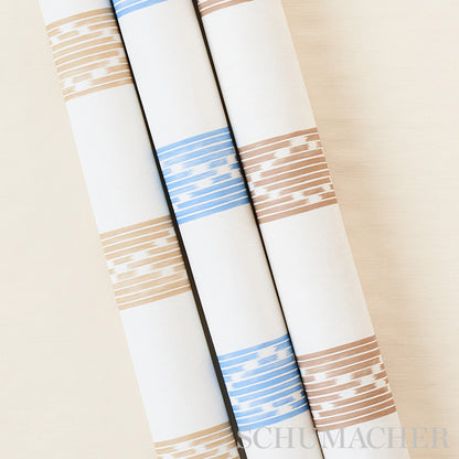 Three white wallpaper rolls with beige and blue striped bands, leaning together on a pale beige wall.
