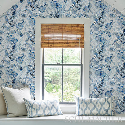 Window with bamboo shade, surrounded by blue floral wallpaper; white sill with beige and blue patterned cushions.