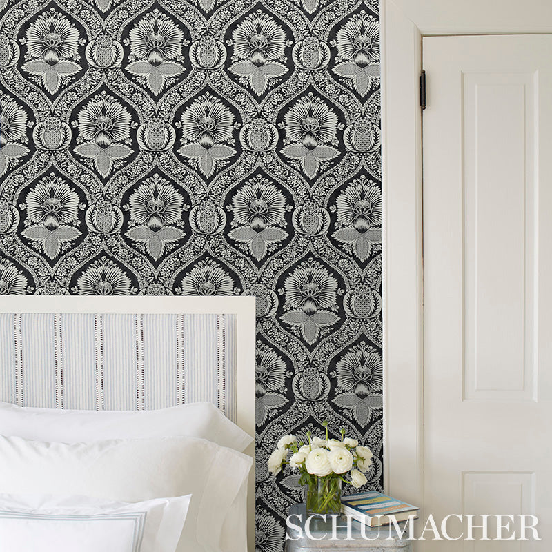 Black-and-white damask wallpaper behind a white striped headboard bed with white bedding and a vase of white flowers.